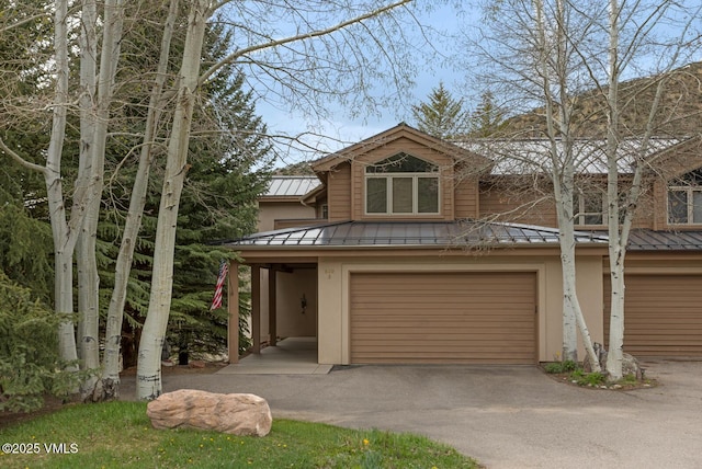 view of front of property with a standing seam roof, an attached garage, metal roof, stucco siding, and driveway