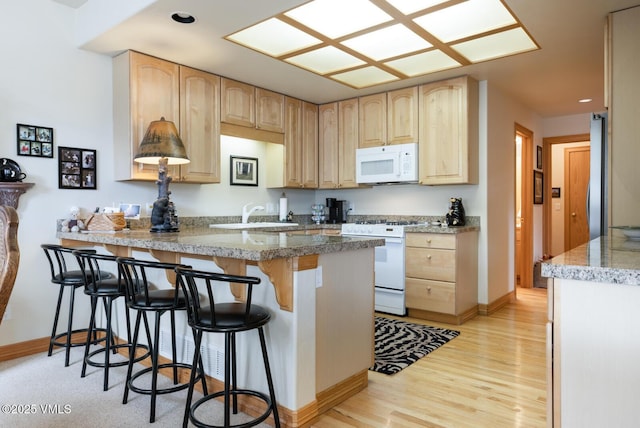 kitchen with white appliances, light brown cabinets, a peninsula, a sink, and a breakfast bar