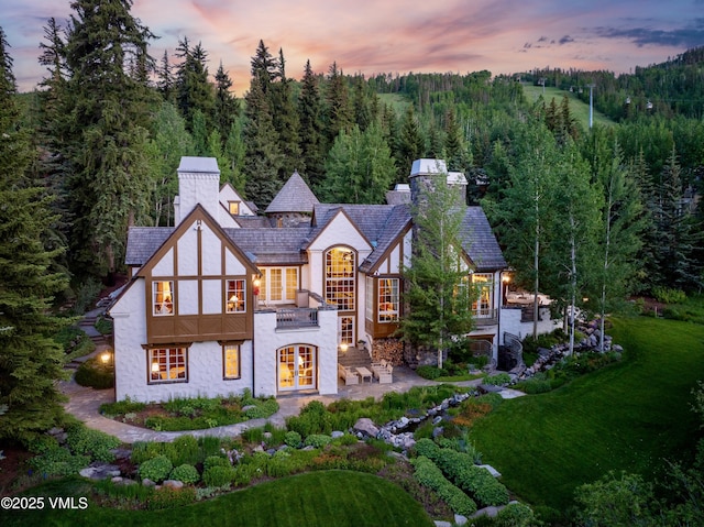 443 Beaver Dam Rd, Vail, CO 81657 - back of house at dusk with french doors, a chimney, stucco siding, and a forest view