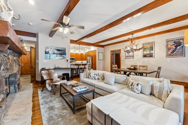 205 Bear Paw Unit B102, Avon, CO 81620 - living room featuring light wood-type flooring, ceiling fan with notable chandelier, a stone fireplace, and beamed ceiling