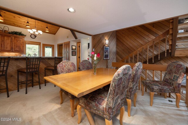 carpeted dining area with lofted ceiling, a chandelier, and wood walls