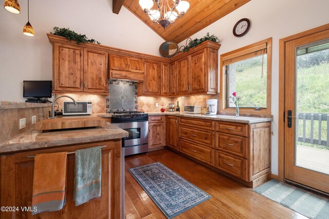 kitchen featuring decorative light fixtures, lofted ceiling with beams, tasteful backsplash, stainless steel gas range oven, and light hardwood / wood-style flooring