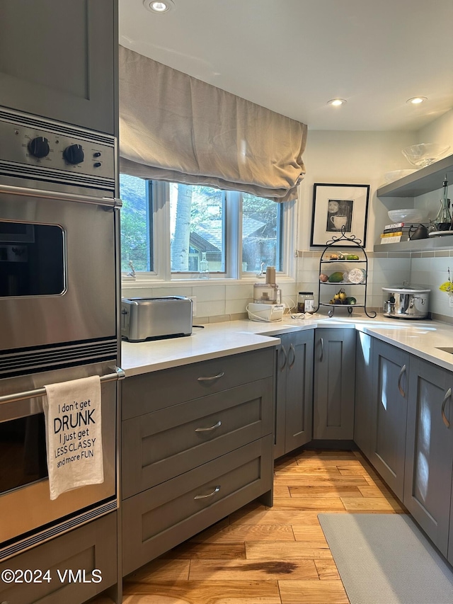 kitchen with gray cabinetry, double oven, backsplash, and light wood-type flooring