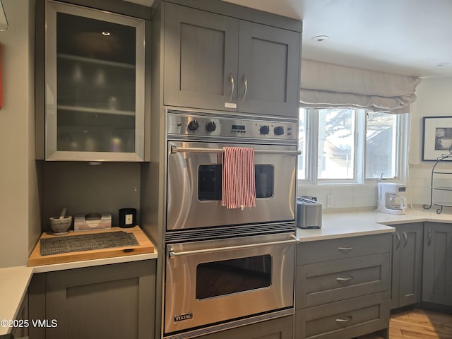 kitchen with tasteful backsplash, gray cabinetry, double oven, and light hardwood / wood-style flooring