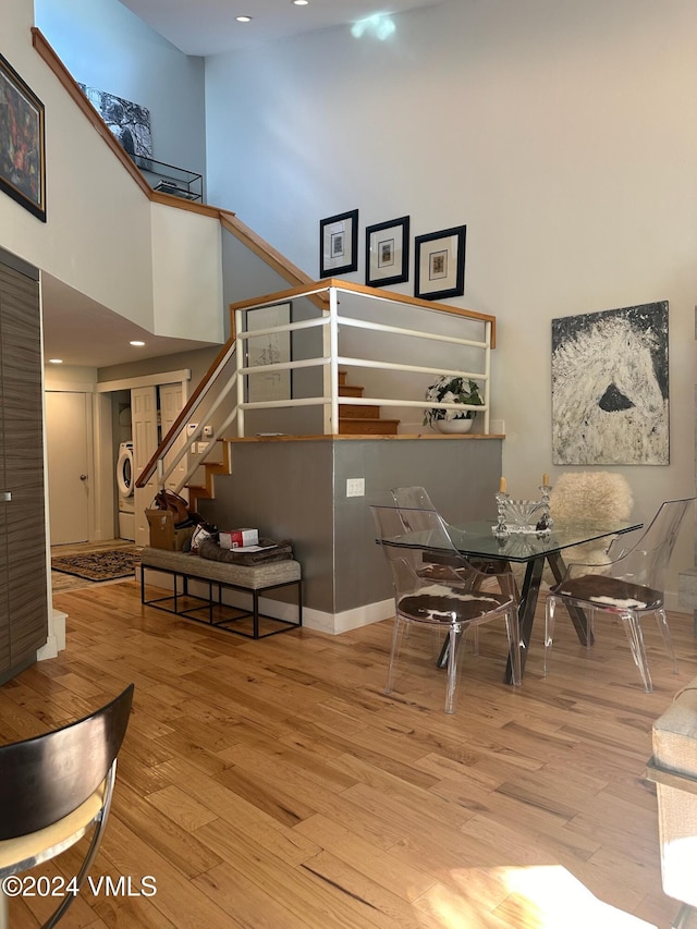 dining space featuring a towering ceiling, stacked washer / drying machine, and light hardwood / wood-style floors