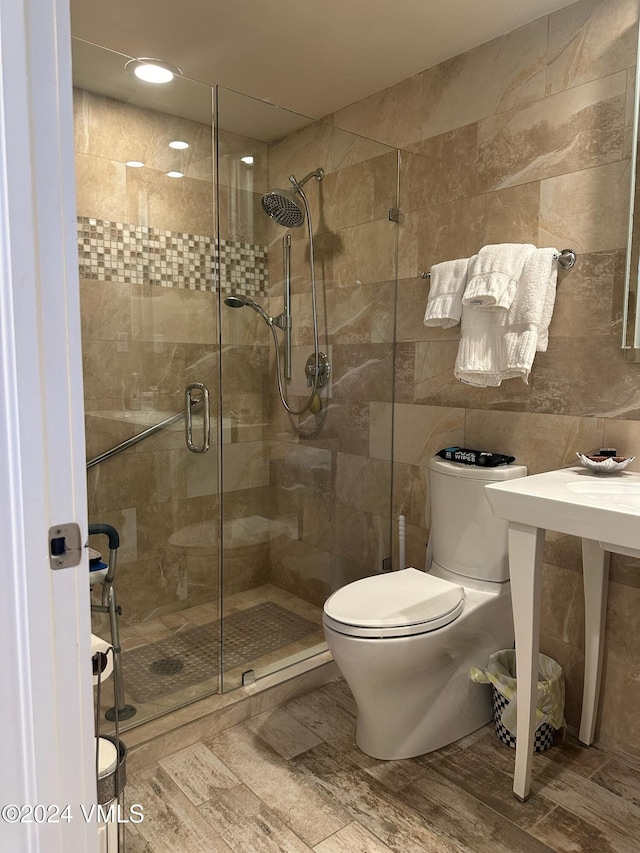 bathroom with tile walls, a shower with door, and toilet