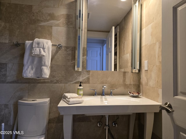 bathroom with toilet, sink, decorative backsplash, and tile walls