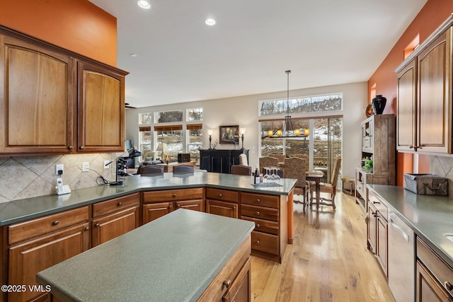 kitchen featuring a peninsula, a healthy amount of sunlight, light wood-style floors, stainless steel dishwasher, and tasteful backsplash