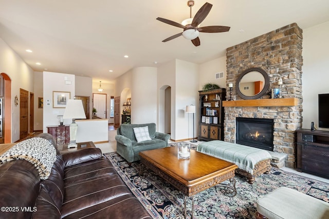 living area featuring visible vents, arched walkways, a ceiling fan, a stone fireplace, and recessed lighting