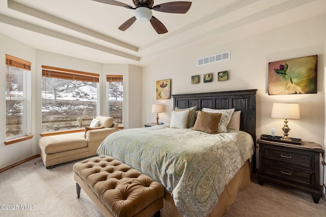 carpeted bedroom featuring a tray ceiling, a ceiling fan, visible vents, and baseboards