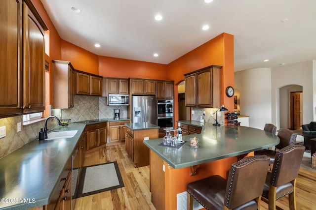 kitchen featuring arched walkways, stainless steel appliances, dark countertops, a sink, and a kitchen island