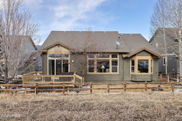 rear view of house with roof with shingles, fence, and a wooden deck