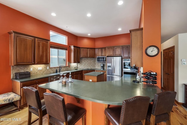 kitchen with appliances with stainless steel finishes, light wood-type flooring, a peninsula, and tasteful backsplash