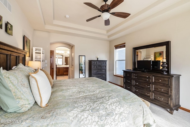 bedroom with baseboards, visible vents, arched walkways, light colored carpet, and a tray ceiling