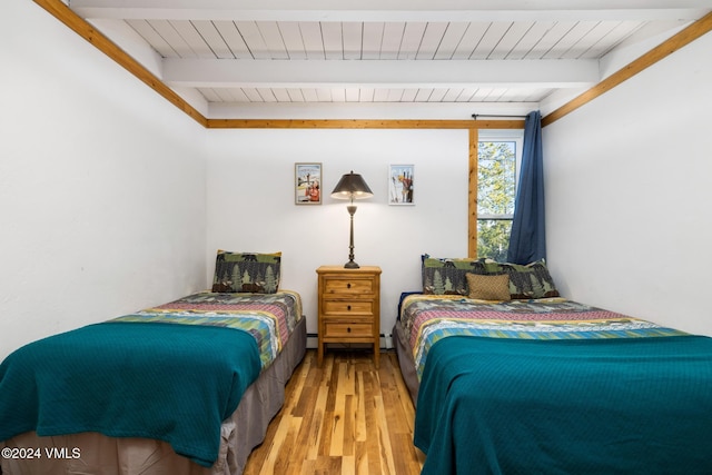 bedroom with beam ceiling, hardwood / wood-style floors, and a baseboard heating unit