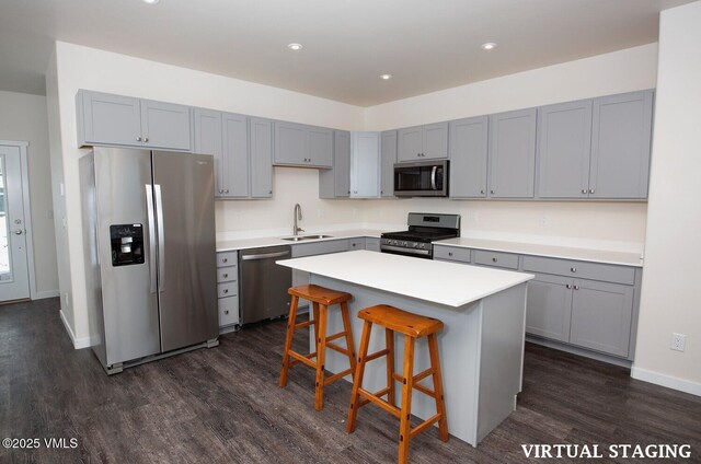 kitchen with sink, appliances with stainless steel finishes, a kitchen breakfast bar, dark hardwood / wood-style floors, and a center island