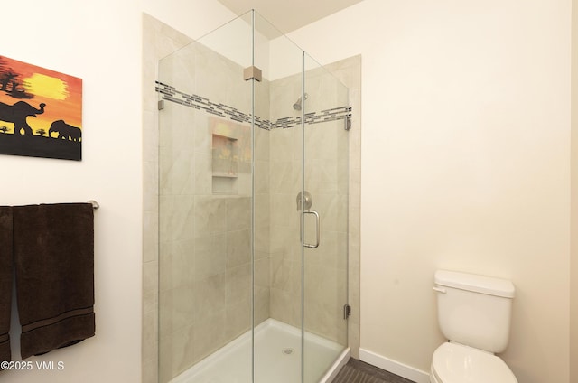 bathroom featuring toilet, a shower stall, and baseboards