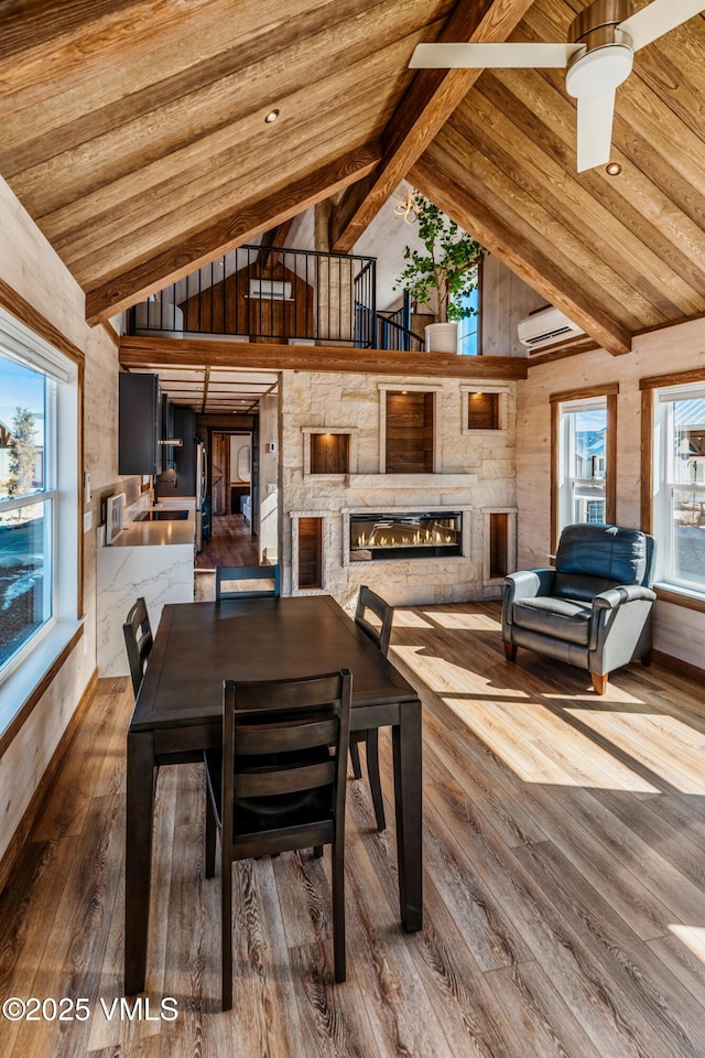 dining area featuring a wall unit AC, a wealth of natural light, wood ceiling, a stone fireplace, and wood finished floors