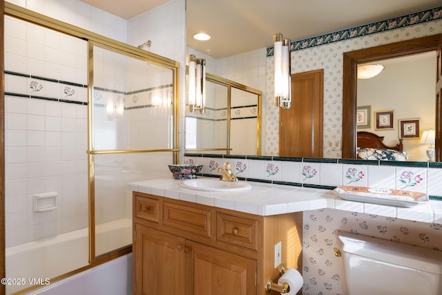 bathroom featuring toilet, wallpapered walls, vanity, and bath / shower combo with glass door