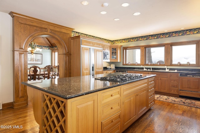 kitchen with wood finished floors, a kitchen island, dark stone counters, recessed lighting, and built in appliances