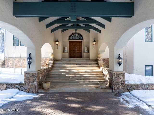 snow covered property entrance with covered porch, stucco siding, and french doors