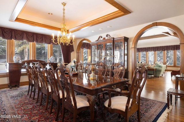 dining area with arched walkways, a notable chandelier, a tray ceiling, and wood finished floors