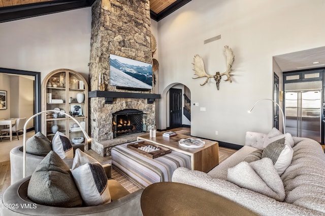 living area with visible vents, a fireplace, a towering ceiling, wood finished floors, and arched walkways