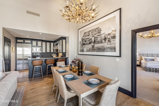 dining area featuring visible vents, light wood-style flooring, a high ceiling, an inviting chandelier, and baseboards