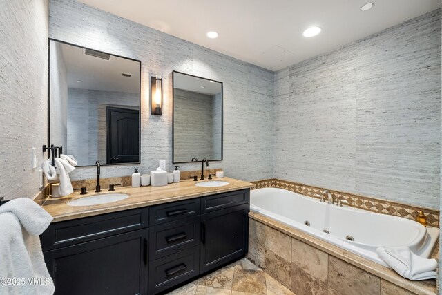 bathroom featuring double vanity, a tub with jets, tile walls, and a sink