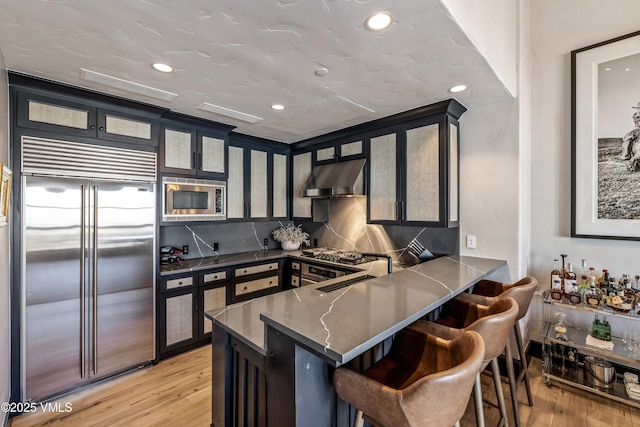 kitchen featuring under cabinet range hood, a breakfast bar area, light wood-type flooring, and built in appliances