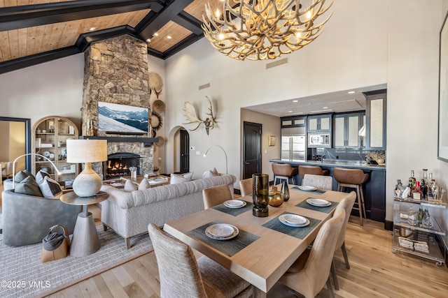 dining area with visible vents, beam ceiling, a stone fireplace, a notable chandelier, and light wood-type flooring