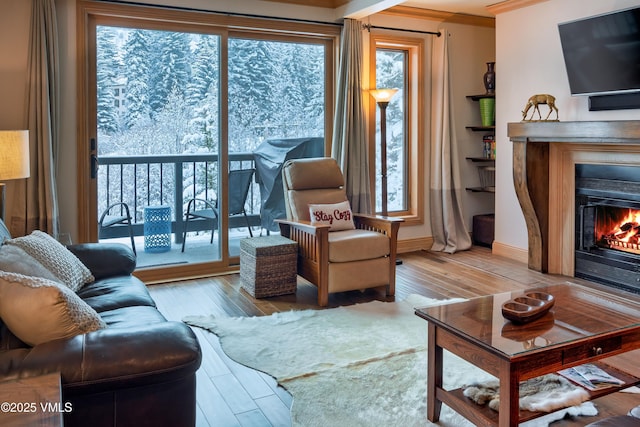 living room featuring a warm lit fireplace, crown molding, baseboards, and wood finished floors