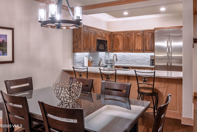 kitchen with black microwave, a peninsula, a sink, backsplash, and stainless steel built in refrigerator