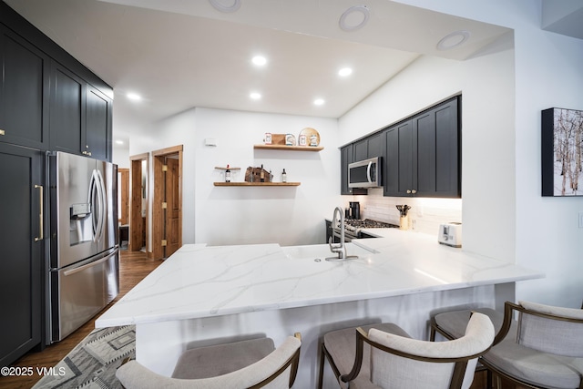 kitchen with tasteful backsplash, appliances with stainless steel finishes, dark hardwood / wood-style floors, kitchen peninsula, and light stone countertops