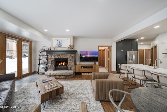 living room with a stone fireplace, sink, and dark wood-type flooring