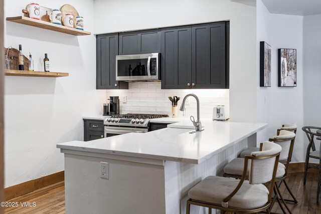 kitchen with a kitchen bar, kitchen peninsula, stainless steel appliances, light stone countertops, and backsplash