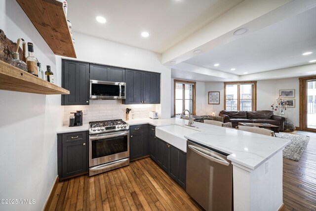 kitchen with light stone counters, appliances with stainless steel finishes, kitchen peninsula, and sink