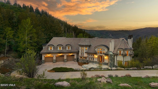 460 El Mirador Rd, Edwards, CO 81632 - back of property at dusk featuring a chimney, driveway, a mountain view, stucco siding, and a view of trees