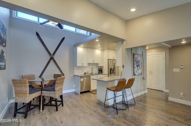 kitchen featuring stainless steel appliances, decorative backsplash, white cabinets, a sink, and wood finished floors