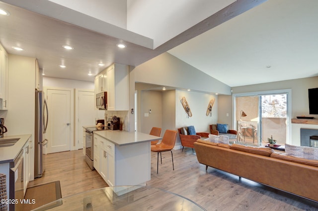 kitchen featuring vaulted ceiling with beams, light wood-style flooring, stainless steel appliances, and open floor plan