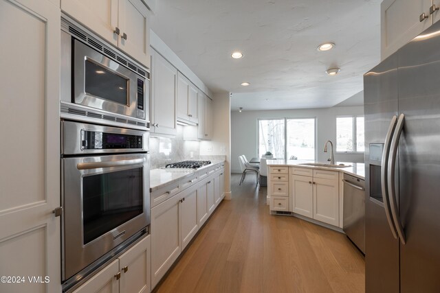 kitchen with sink, white cabinetry, light wood-type flooring, stainless steel appliances, and backsplash