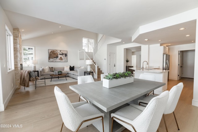 dining space with sink, light hardwood / wood-style flooring, and vaulted ceiling