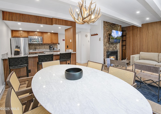 dining space with a notable chandelier, recessed lighting, light wood-style flooring, a stone fireplace, and beamed ceiling