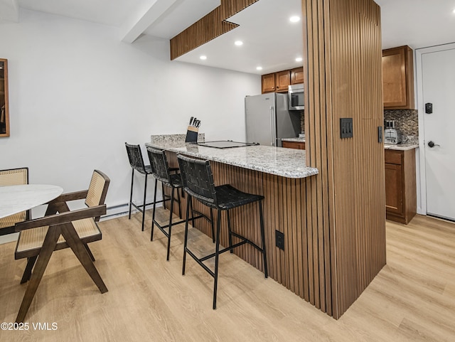 kitchen featuring brown cabinets, stainless steel appliances, backsplash, light wood-style floors, and a kitchen breakfast bar