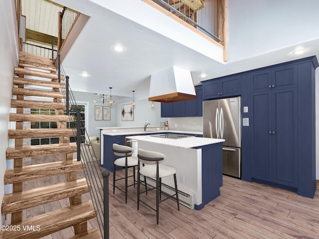 kitchen featuring a peninsula, blue cabinetry, freestanding refrigerator, light wood-style floors, and exhaust hood
