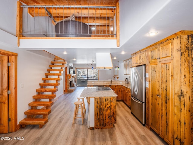 kitchen featuring freestanding refrigerator, a sink, a towering ceiling, and light wood finished floors