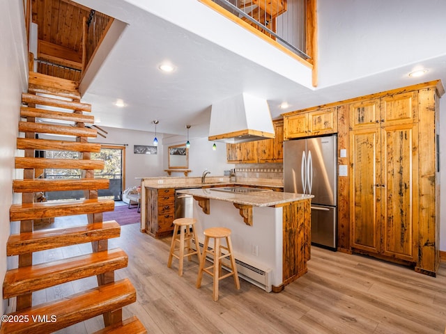 kitchen with tasteful backsplash, light wood-style flooring, freestanding refrigerator, a peninsula, and premium range hood