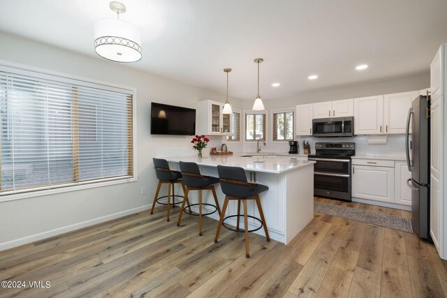 kitchen featuring decorative light fixtures, stainless steel appliances, kitchen peninsula, and white cabinets