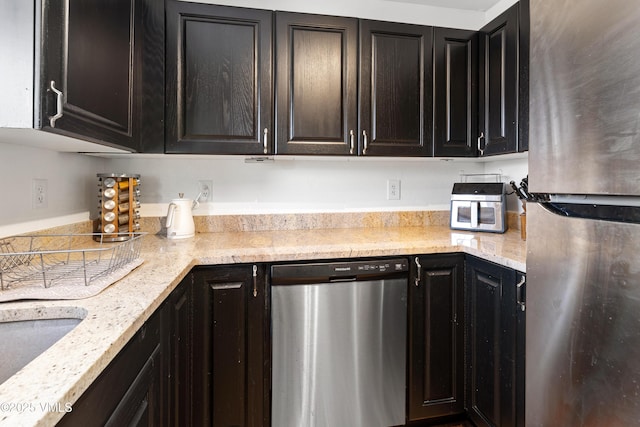 kitchen featuring stainless steel appliances, light stone counters, a sink, and dark cabinets