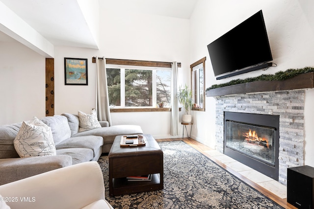 living room featuring vaulted ceiling, a stone fireplace, baseboards, and wood finished floors